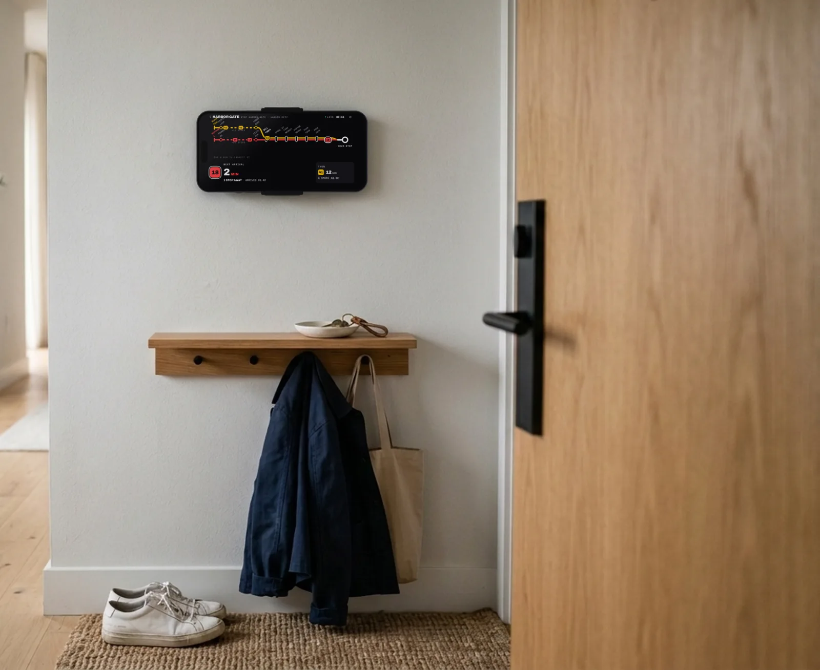 An entryway with the front door closed and an iPhone mounted sideways on the wall beside it, showing the board: line 18 in 2 minutes